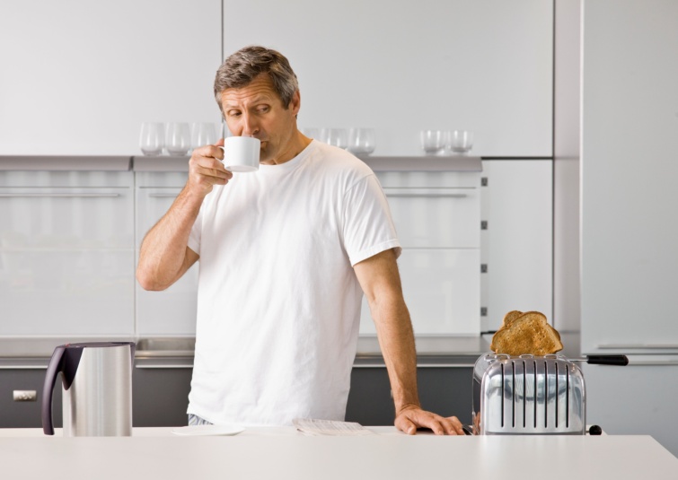 Kávét ivó idős férfi néz egy kenyérpirítót.