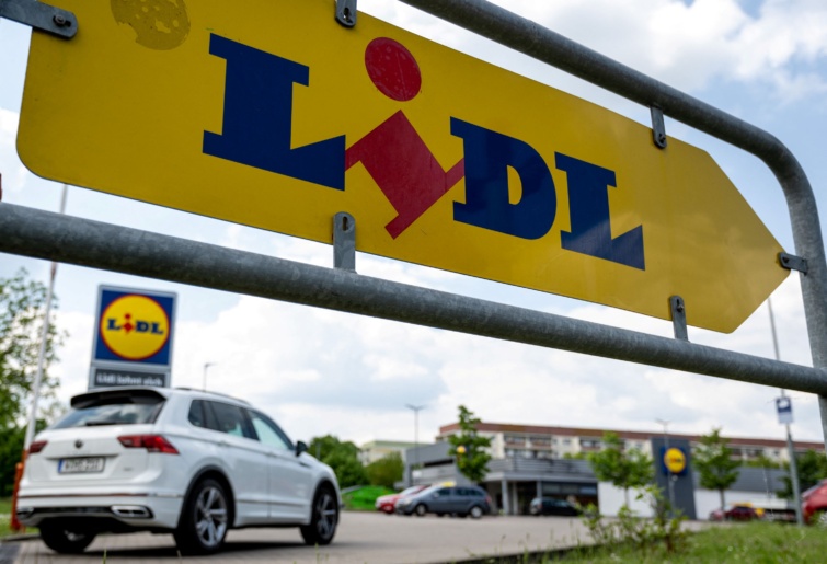 A Lidl logója egy jelzőtáblán az áruház előtt, amint egy autó halad az üzlet felé.