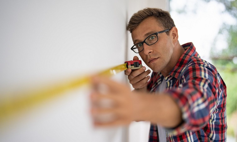 Egy férfi a falon mér mérőszalaggal.