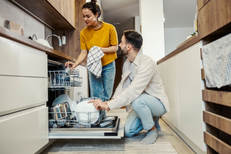 Mosolygó férfi és nő pakolják be a mosogatógépet.