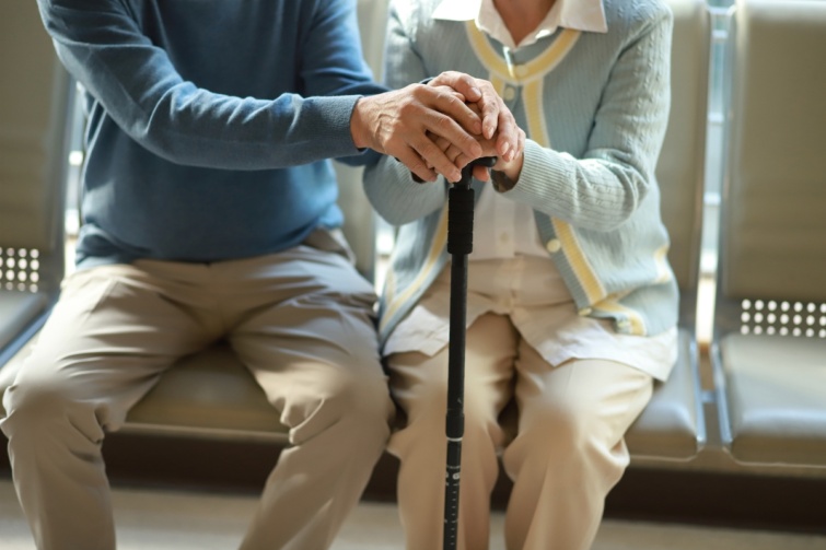 Nyugdíjas pár kéz a kézben, botra támaszkodva