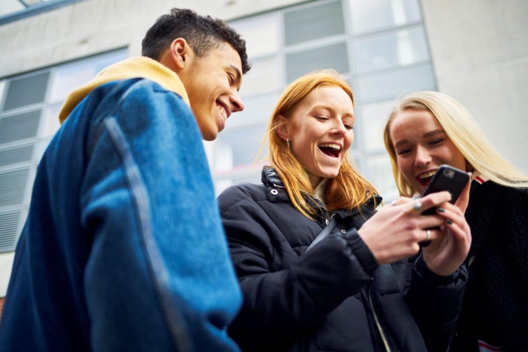 okostelefon Startlap Vásárlás Mosolygó fiatalok néznek egy okostelefont.