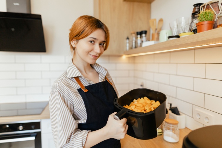 Mosolygó nő sült krumplival az airfryer tálcájában.