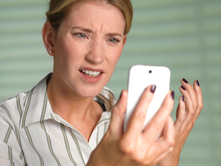 Ideges nő egy okostelefon képernyőjét nézi.