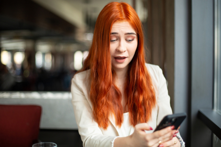 Vöröshajú nő kérdően nézik a telefonjára
