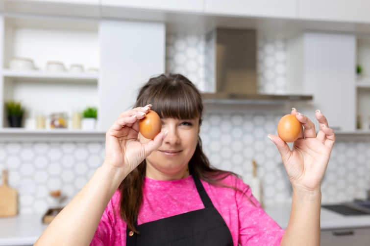 Kötényes nő tojásokat tart a kezében.