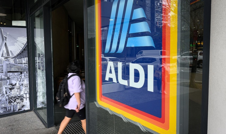 Egy hátizsákos, rövidnadrágos nő belép egy Aldi-üzlet bejáratán.