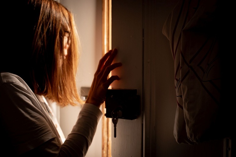 Someone rings doorbell in the middle of the night and a woman opens the door Startlap Vásárlás Egy nő kikémlel a résnyire nyitott ajtón.