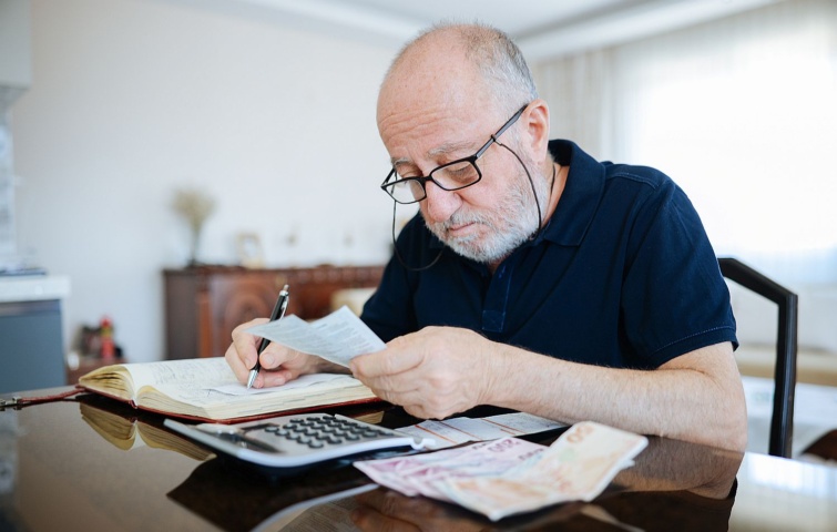 Anxious senior man managing finances holding cash and using calculator at home Startlap Vásárlás Idős, szemüveges férfi ír.