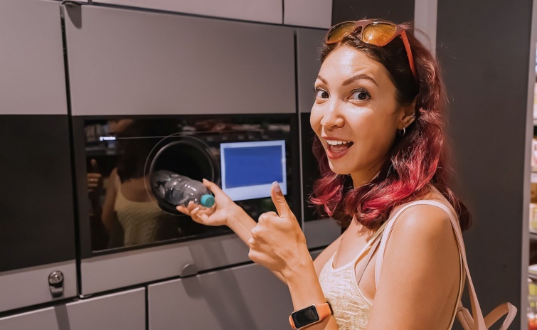Happy student girl hands over a plastic beverage bottle for recycling to automated machine Eco friendly lifestyle and cashback Startlap Vásárlás Egy fiatal nő bedob egy palackot a visszaváltó automatába.