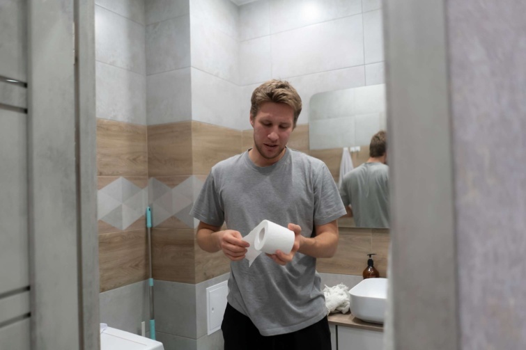 wc papírt nézegető férfi a fürdőben