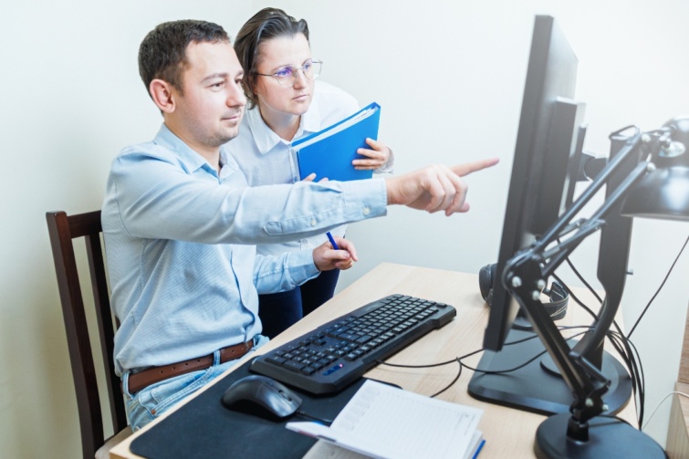 ferfinolaptop Startlap Vásárlás Egy férfi a monitorra mutat, miközben kolléga együtt figyel az irodai asztalnál.