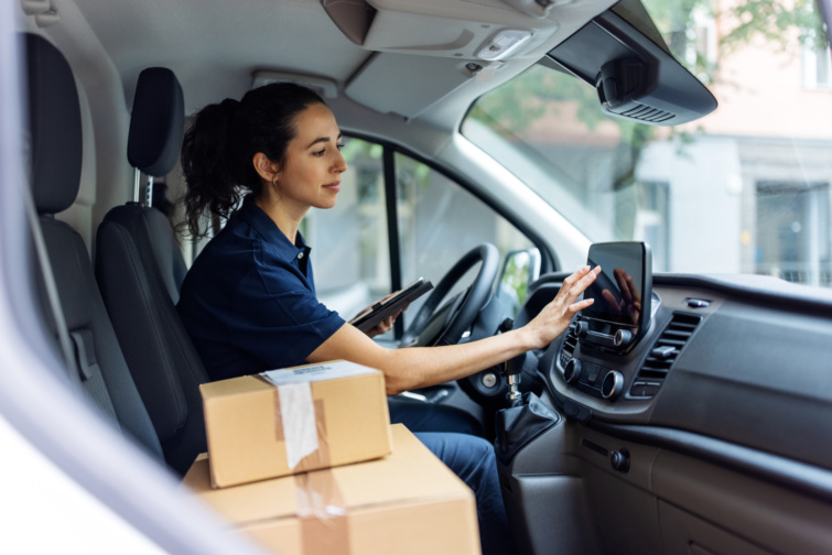 Fiatal lány tehergépjárműben navigációs rendszert használ, mellette dobozokkal