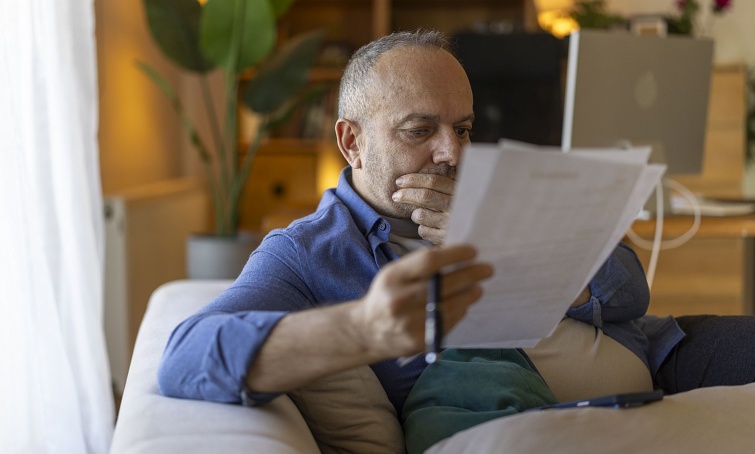 Mature man feeling stressed reviewing financial documents at home Startlap Vásárlás Egy idős férfi papírlapokat tart a kezében és olvas.