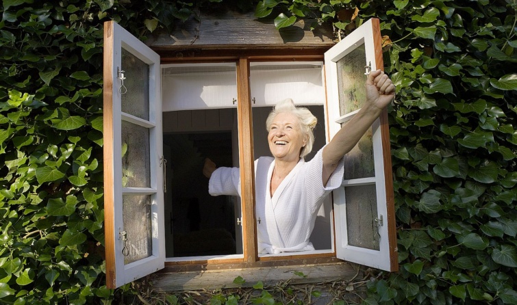 Senior woman wearing rollers in hair opening window smiling Startlap Vásárlás Idős, vidám nő kihajol a nyitott ablakon, a ház fala borostyánnal befutva.