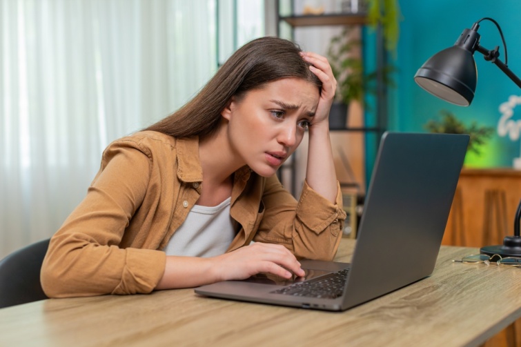 Young woman frowning at laptop reading worrying news showing stress and fatigue in late work session Startlap Vásárlás Fiatal nő otthon ül az asztalnál, szomorú híreket olvas a laptopján