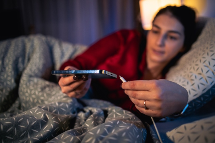 Fiatal nő éjjel az ágya mellett töltőre dugja a telefonját