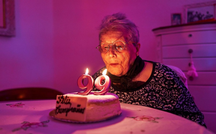 Old woman blowing out the candles of a birthday cake Startlap Vásárlás 99 éves nő elfújja a gyertyát a születésnapi tortáján.