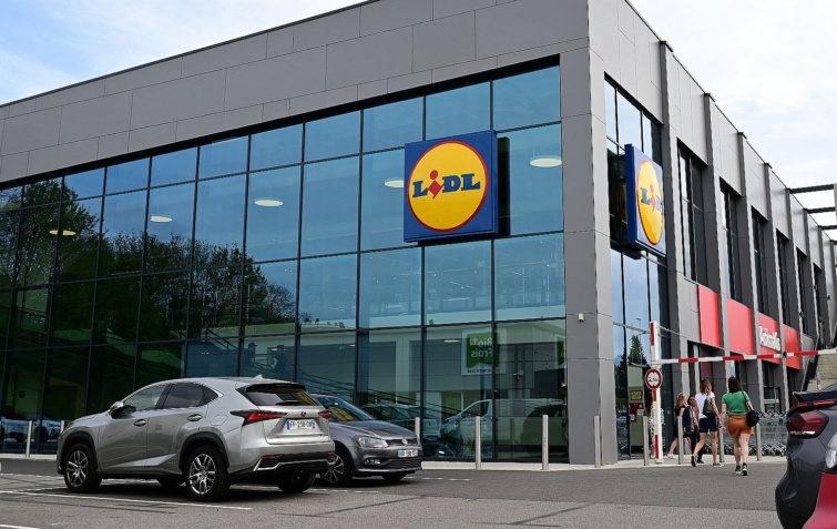 Egy Lidl bolt, a parkolója autókkal és vásárlókkal.