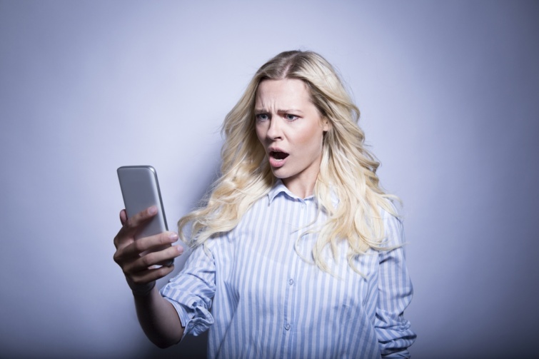 Mérgesen, csodálkozva nézi egy nő a mobiltelefonja képernyőjét