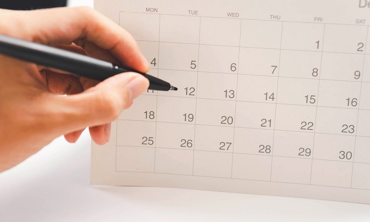 Event planner checking yearly schedule on mobile phone with calendar and desk planner organizing tasks managing events and planning work efficiently in a modern office setting Startlap Vásárlás Egy filctollat tartó kézfej egy naptárlap előtt.