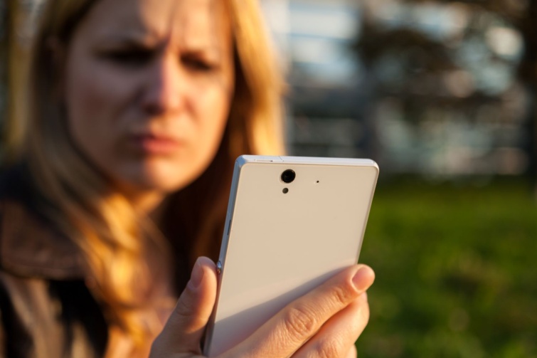 telefon pötty Startlap Vásárlás Ráncolt szemöldökű nő nézi zavartan a telefonját.