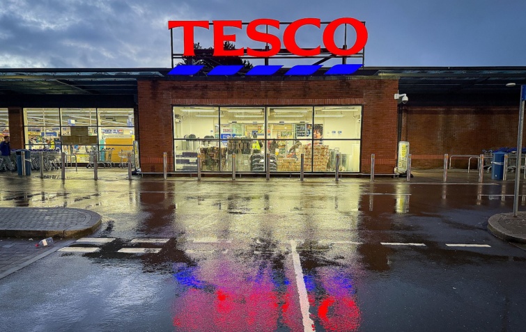 UK Supermarket Retailer Tesco Startlap Vásárlás Egy világító Tesco logó egy üzleten sötétben, esőben.