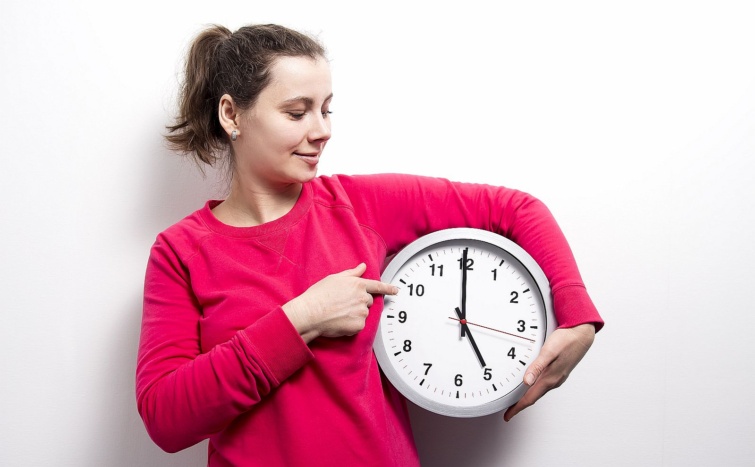 brunette girl is holding clock and points to hands of clock on white background concept of time Watch stop and control time Young woman holds round clock in hands Startlap Vásárlás Piros pulóveres fiatal nő egy kezében tartott faliórára mutat