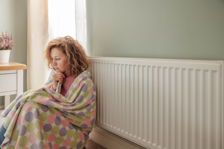 A woman wrapped in a blanket trying to keep warm by sitting by a heating radiator Startlap Vásárlás radiátor előtt takaróban ülő nő