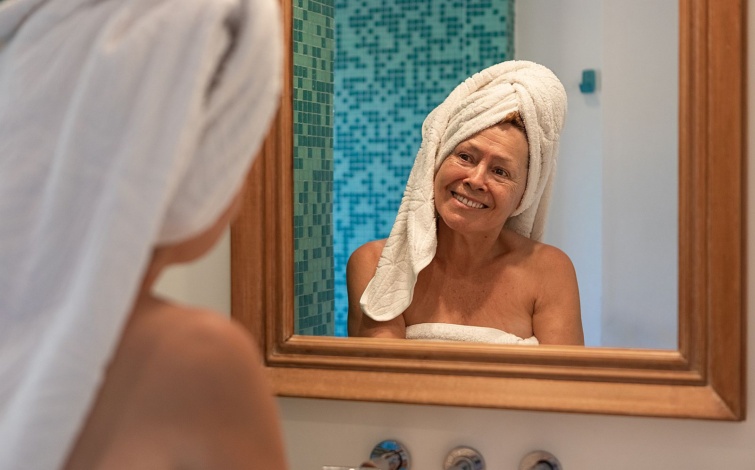 Senior lady doing her facial beauty routine Startlap Vásárlás Törölközőbe csavart hajú idős nő mosolyog a tükörből.