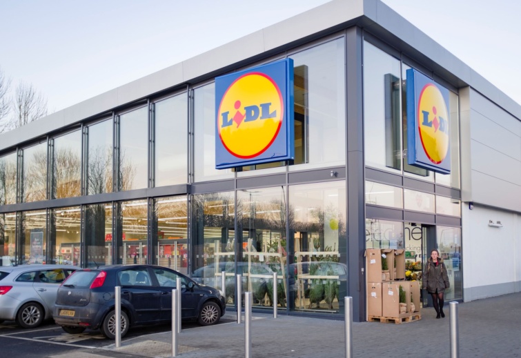Lidl szupermarket külső nézete, a bejárat előtt egy vásárló nővel